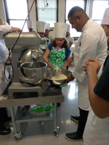 A Teen Squad participant helps a chef from the Genesis Center add ingredients to a dish