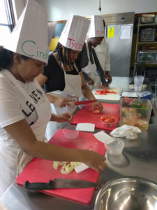 Teen Squad culinary arts program participants dice onions and peppers in a kitchen