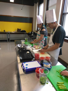 Teen Squad culinary arts program participants dice onions and peppers in a kitchen