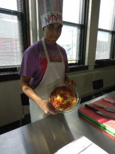 A Teen Squad member holding up a quiche he prepared as part of the culinary arts program