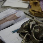 Gold fabric sitting on top of a book and a sketch of a 1920s flapper dress