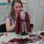 A Teen Squad member works on a pink dress with a red cape on a miniature dress form