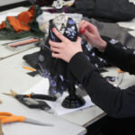 A Teen Squad member works on a black and violet colored dress on a miniature dress form