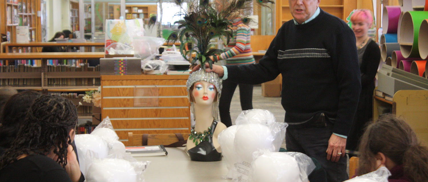 A mentor displaying an elaborate peacock headdress on a mannequin head