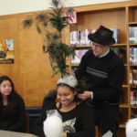 A Teen Squad member trying on an elaborate peacock headdress with the help of a mentor