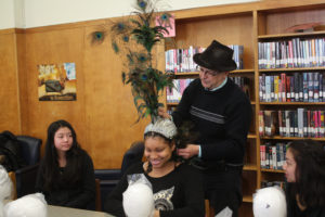 A Teen Squad member trying on an elaborate peacock headdress with the help of a mentor