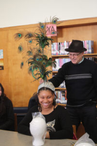 A Teen Squad member trying on an elaborate peacock headdress with the help of a mentor