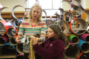 A mentor and a Teen Squad member discuss a headdress in progress