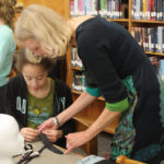 A Teen Squad member and a mentor discuss preparing a length of fabric for a headddress