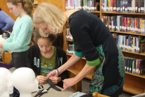 A Teen Squad member and a mentor discuss preparing a length of fabric for a headddress