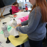 A Teen Squad member works on a dress on a miniature dress form