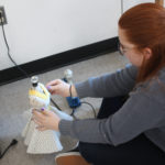 A Teen Squad member hot glues material on a dress on a miniature dress form