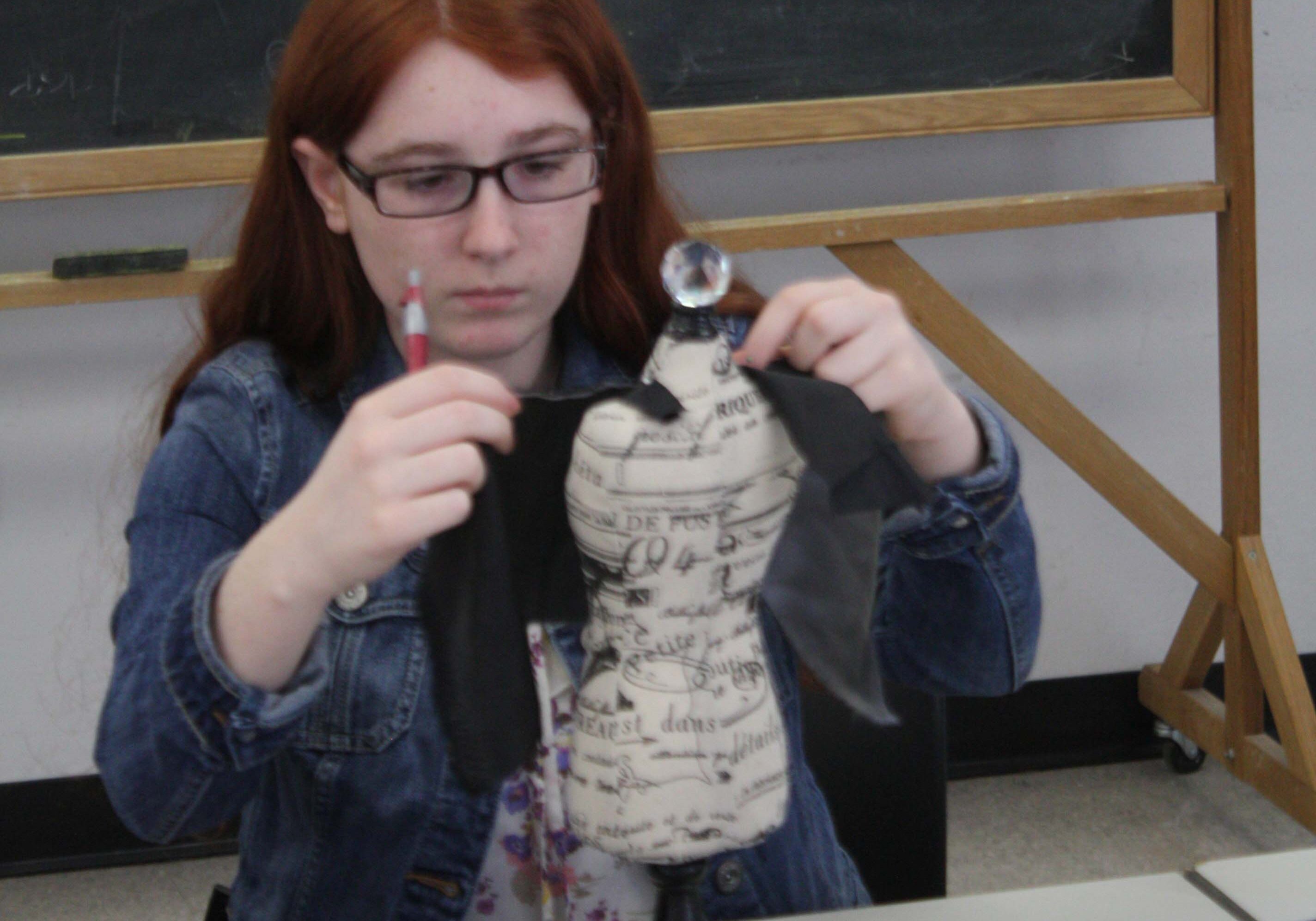 A participant in a teen program designs a dress on a miniature dress form